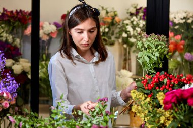 Genç beyaz çiçekçi buket yapıyor. Çiçekleri düzenleyen deneyimli bayan.