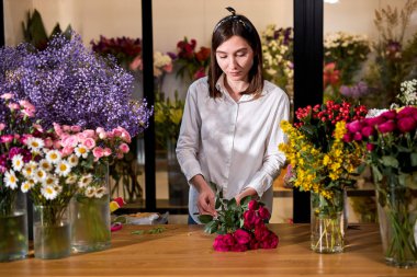Çiçekçide buket yaparken gül düzenleyen güzel bir kadın.