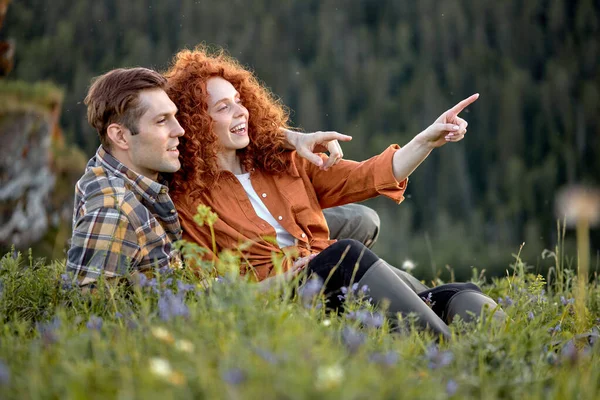 Romantikus fiatal pár, akik a réten ülnek a hegyekben.. — Stock Fotó