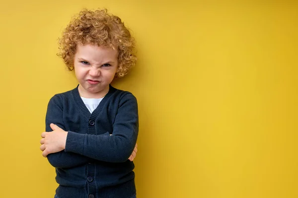Lockigt plågade barn pojke med armar vikta poserar vid kameran, isolerad på gul — Stockfoto