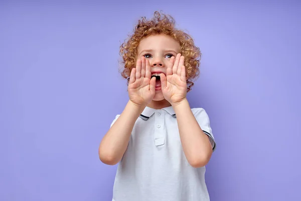 Liten barn skriker i häpnad mot lila bakgrund, höja händerna upp — Stockfoto