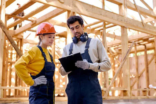 Två män och kvinnor i uniform och hjälm utforskar konstruktionsdokumentation — Stockfoto