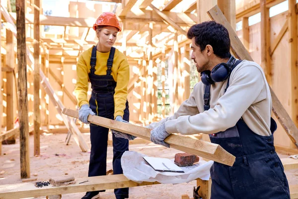 Amical homme et femme en uniforme travaillant ensemble sur le chantier de construction en bois — Photo