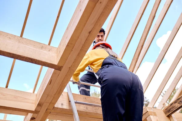 Two contractors climb to the roof of wooden building house on stepladder — Stock Photo, Image