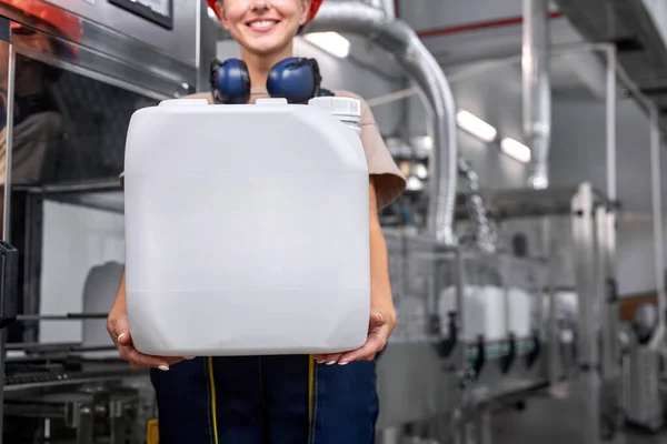 Gekapte vrouw in uniform met witte plastic vaten die chemicaliën bevatten in de fabriek — Stockfoto