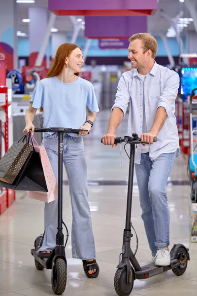 Retrato de pareja agradable satisfecho en scooters eléctricos en el interior de la tienda —  Fotos de Stock