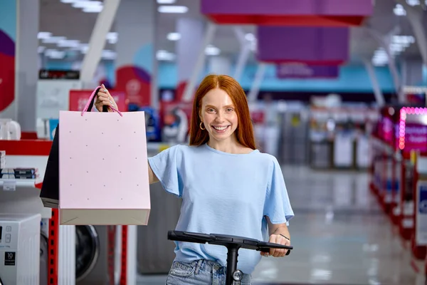 Mulher segurar mão sacos de compras mulher depois de fazer compras em scooter chute elétrico — Fotografia de Stock