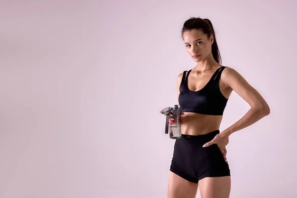 Női modell pózol vizes palackkal, mielőtt fitness stúdió háttér — Stock Fotó