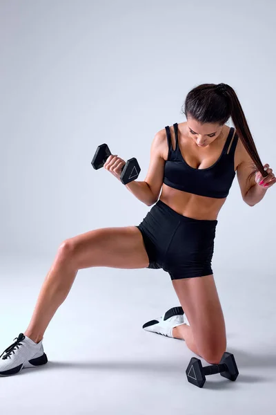 Atraente jovem mulher fitness fazendo treino com halteres sentados no chão isolado. — Fotografia de Stock