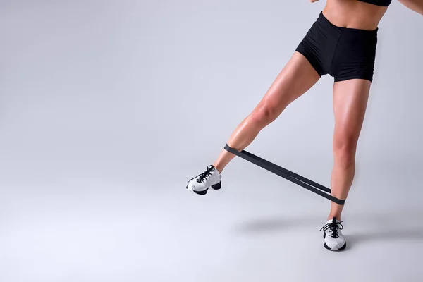 Mujer en forma recortada está haciendo entrenamiento de piernas usando banda de resistencia elástica para la aptitud — Foto de Stock