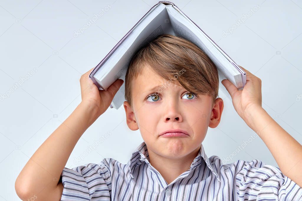 Crying Child Boy with Book on Head on White Studio Background Copy Space.