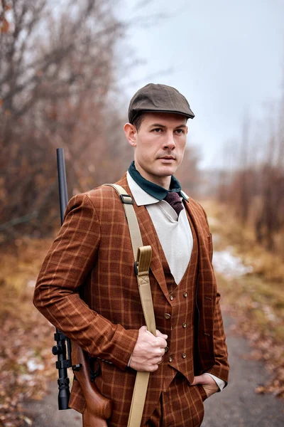 Jistý muž lovec se chystá lovit, oblečený v hnědém stylovém obleku a klobouku — Stock fotografie