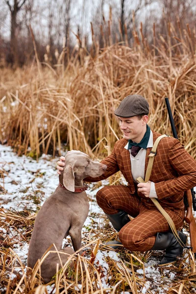 Genç adam av tüfeği tutuyor ve köpeği okşuyor, ormanda, avlanmaya geliyor.. — Stok fotoğraf