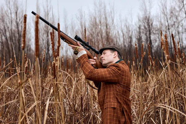 Caçador vestindo terno marrom na moda e chapéu à espera do pássaro, apontando rifle up — Fotografia de Stock