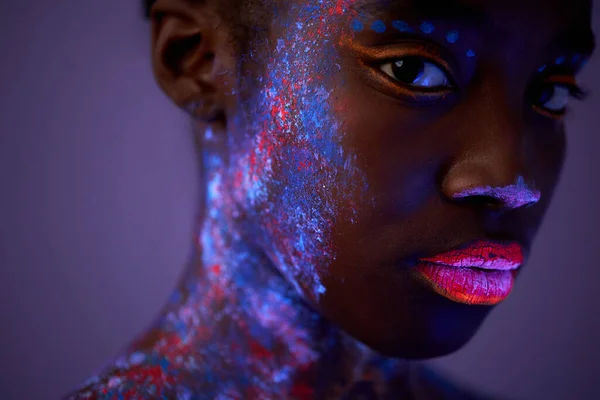 Svart kvinna med neon make-up kropp konst poserar tittar på kameran, isolerad på lila — Stockfoto