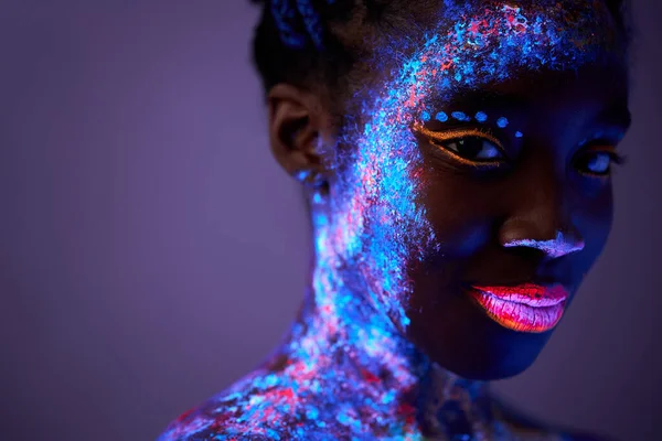 Schwarze Dame mit neon geschminktem Körper posiert in die Kamera, isoliert auf lila — Stockfoto