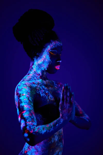 Schwarzes Gebet mit fluoreszierender Körperkunst, die in der Dunkelheit leuchtet, bunte ethnische Abdrücke auf nackter Haut — Stockfoto