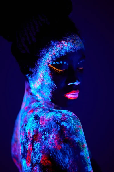 Mujer negra con el arte del cuerpo UV que brilla en la oscuridad, impresiones coloridas en piel desnuda — Foto de Stock