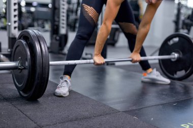 Ağır ağırlık çubuğuyla egzersiz yapan kırpılmış genç bir vücut geliştirme ustası. Fitness kadını
