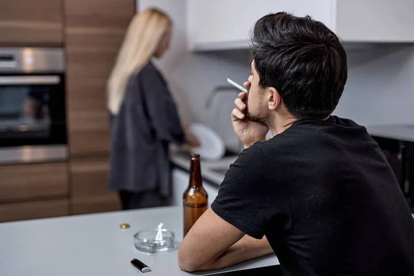 부엌에서 불화를 겪는 부부, 남자는 여자가 요리를 하는 동안앉아서 흡연을 한다 — 스톡 사진