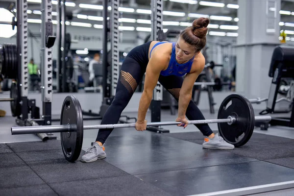 Jong vrouwtje doet zwaar werk squat in de sportschool met lange halter. Vrouw met perfecte buikspieren — Stockfoto
