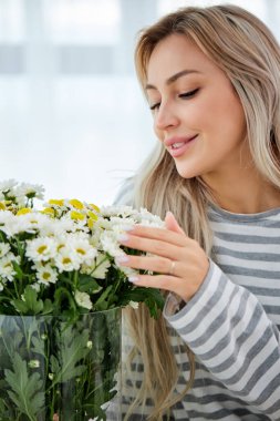Yüzünde narin bir gülümsemeyle evde kır çiçekleriyle çekici bir kadın. Sarışın bayan.