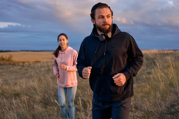 Concentrado chico y señora corriendo juntos durante el atardecer, trotando en el campo — Foto de Stock