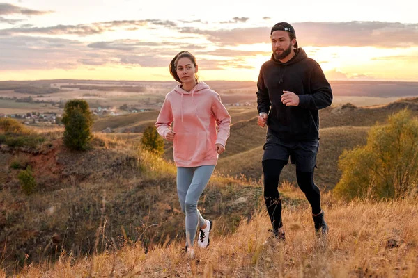 Hombre y mujer corriendo al atardecer o al amanecer a lo largo de montañas de campo, trotando por la mañana — Foto de Stock