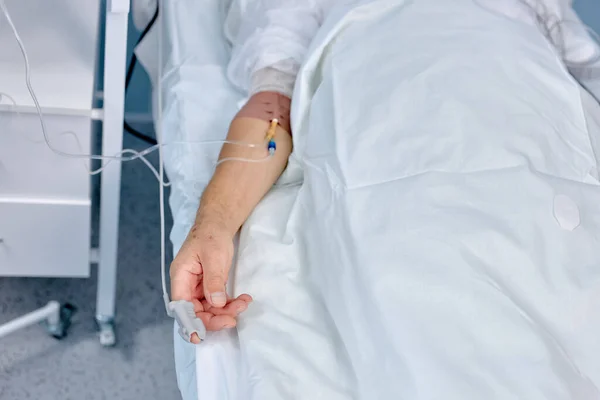 Detailní záběr mužské ruky s injekční stříkačkou v žíle. Starší pacient ležící na lůžku kliniky s katétrem. — Stock fotografie