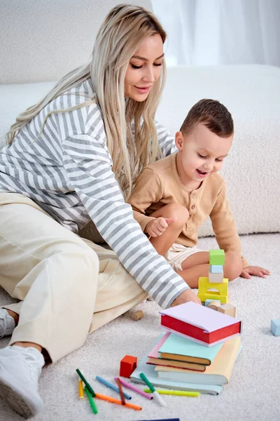 Encantadora madre joven y el niño jugando juego con juguetes en casa juntos, en el suelo. — Foto de Stock