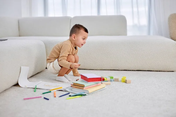 Niño agradable dibuja en el suelo en la sala de estar luminosa. niño feliz dibuja con lápices. — Foto de Stock