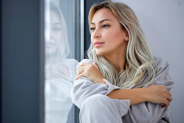 Young beautiful woman posing on the windowsill in room. Casual fashion, beauty. — Stock Photo, Image