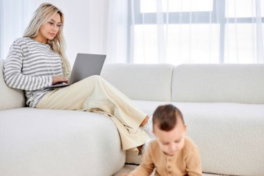 Anne kanepede çalışıyor, çocuk yerde oynarken e-posta yazıyor..