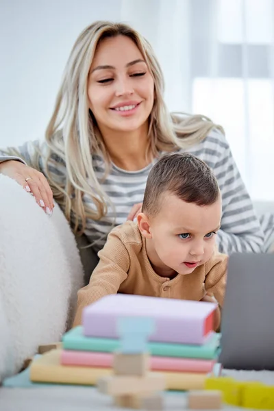 Kavkazská maminka a malý chlapec sedí na pohovce doma sledovat video na moderním notebooku — Stock fotografie