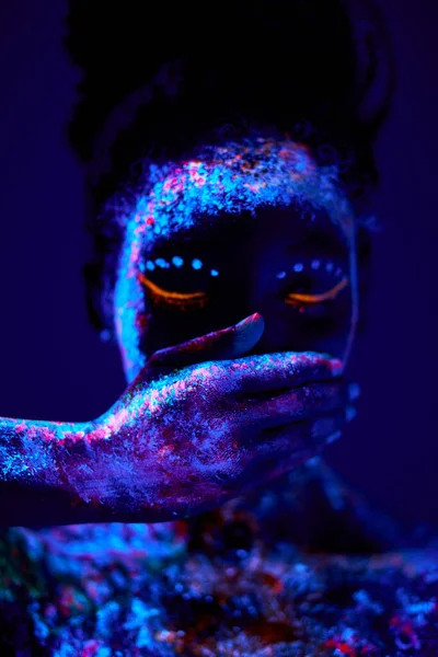 Friedliche schwarze Frau mit kreativen fluoreszierenden Abdrücken auf der Haut, auf dem Körper, Mund schließen — Stockfoto