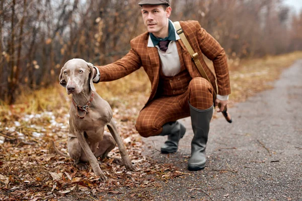 森の中で灰色の狩猟犬とハンター男。屋外で狩りをする男が座って犬を撫でて — ストック写真