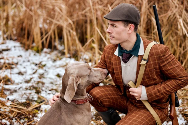 Braconnier avec arme à feu et weimaraner chien de race ami dans la nature, assis ensemble. saison d'automne — Photo