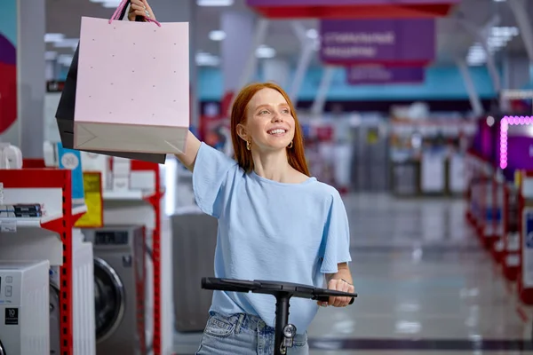 Senhora europeia segurar mão colorido sacos mulher depois de fazer compras em scooter chute elétrico — Fotografia de Stock