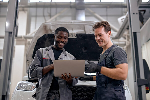 Автомеханики проверяют машину с помощью ноутбука, работают вместе