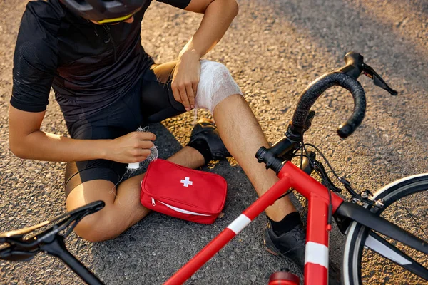 Desportista cortado caiu de bicicleta, usando bandagem de kit de primeiros socorros para ajudar a si mesmo. acidente. — Fotografia de Stock