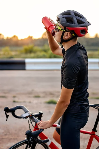 Jovem ciclista cara em roupas de ciclismo e capacete fazendo pausa, água potável — Fotografia de Stock