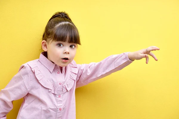 cute little kid girl scared and run expression gesture. isolated yellow background. portrait of frightened child in pink blouse looking at camera with big eyes