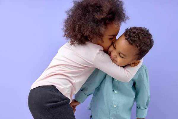 两个快乐的美国黑人兄弟姐妹 姐姐亲吻她的哥哥 孤立的紫色背景 穿着休闲装的漂亮小孩的肖像 男孩和女孩彼此相爱 — 图库照片
