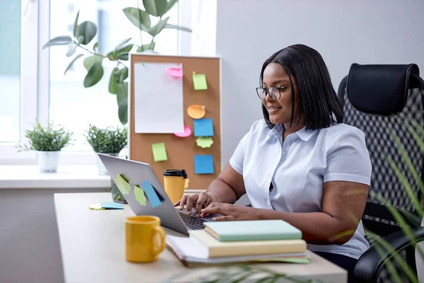 pretty black lady typing on laptop keyboard working online in cozy modern office. american lady with black hair and skin enjoy working alone, managing. startup business. at workplace
