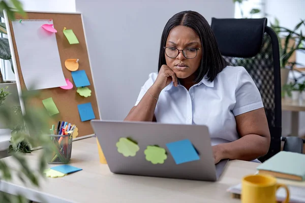 Tired frustrated black woman working on laptop online, overthinking. in office. beautiful lady in formal wear looking at screen misunderstanding. businesswoman at workplace. alone.