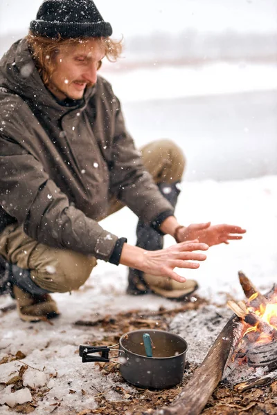 Man warming hands on bonfire in nature in cold season, winter. travel lifestyle photo. adventure active vacations outdoor. Extreme camping. in snowy frozen forest alone, calm and pacified
