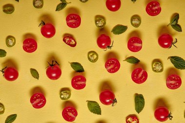 Fresh ripe cherry tomatoes slices scattered isolated on yellow background, fresh bright tomatoes with leafs, flat lay