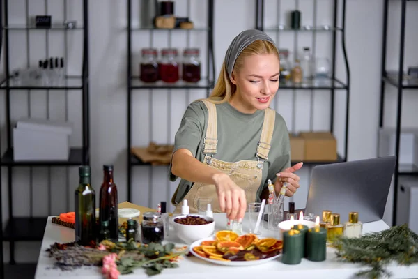 caucasian perfumer take bottle for mixing fragrance and essential oil into another bottles during process of blending the nice scent for making perfect perfume, using laptop, in modern laboratory