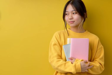 Portrait diligent asian woman hugging books reading education studying learning knowledge smiling positive emotion, in casual yellow shirt, Yellow background isolated studio shot and copy space.