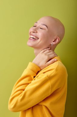 Laughing. young caucasian bald woman posing on green studio background. Human emotions, facial expression,sales, ad concept. Youth culture. Female with alopecia or cancer, after chemotherapy